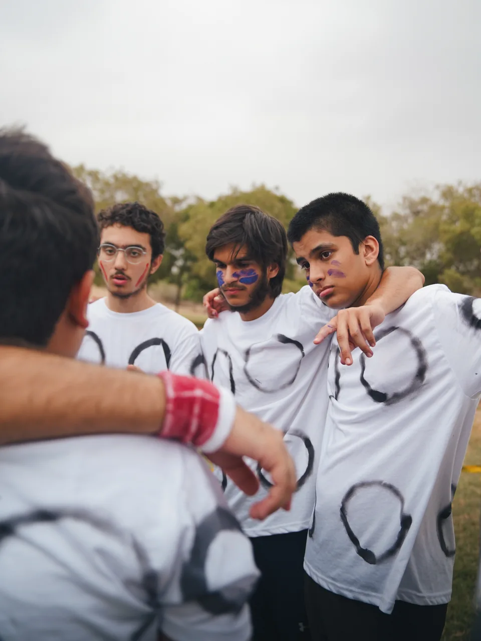 Teammates with face paint listening closely with arms around each other's shoulders.